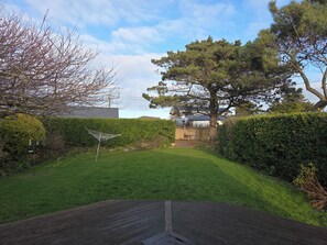 A backyard with a grassy lawn, a wooden deck, and a large tree.