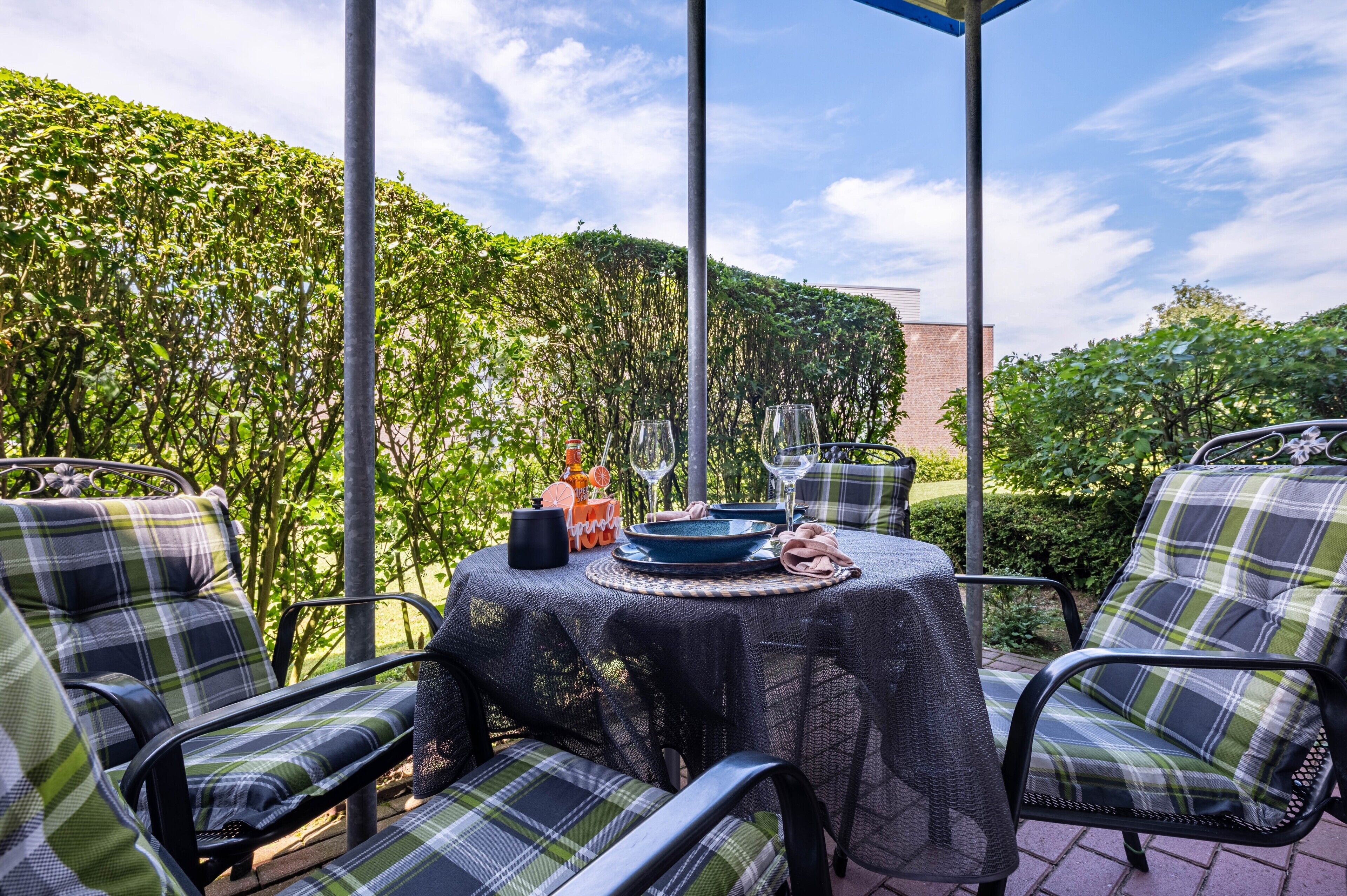 Une terrasse extérieure avec une table dressée pour le repas, entourée de chaises.