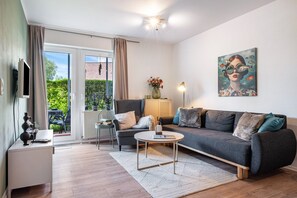 A modern living room with a sofa, armchair, coffee table, and artwork on the wall.