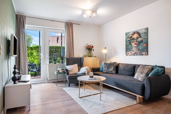 A modern living room with a sofa, armchair, coffee table, and artwork on the wall.
