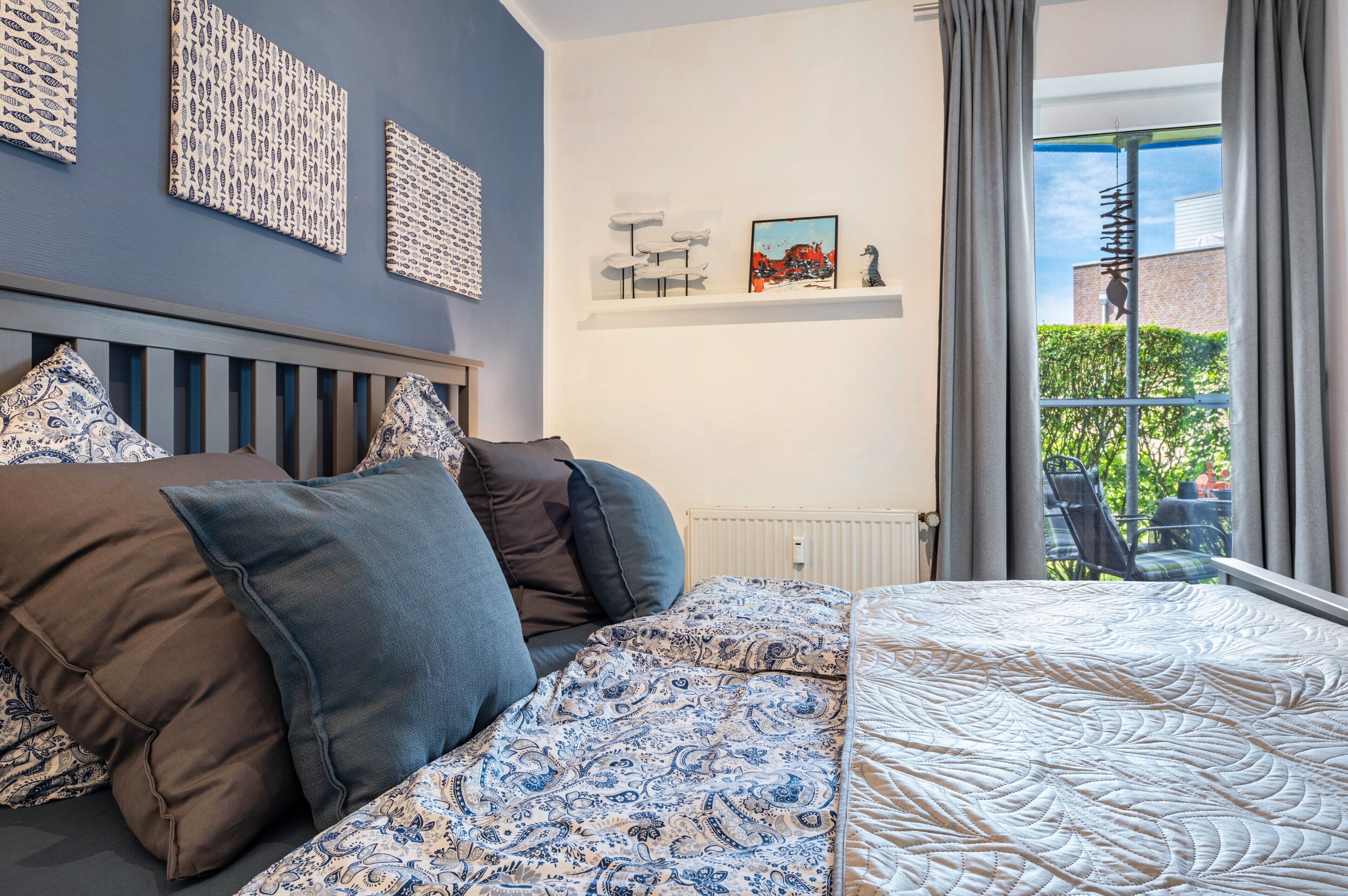 A bedroom with a bed, pillows, a radiator, a window with curtains, and wall art.