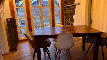 Un comedor con mesa de madera y cuatro sillas, pared de piedra y vista a través de ventanas amplias.