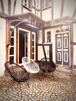Un bâtiment avec des poutres en bois apparentes, une terrasse pavée et deux chaises.