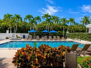 A swimming pool with lounge chairs and umbrellas, surrounded by palm trees and greenery. - Olde Marco Inn #403, Waterfront Island Escape (Marco Island)