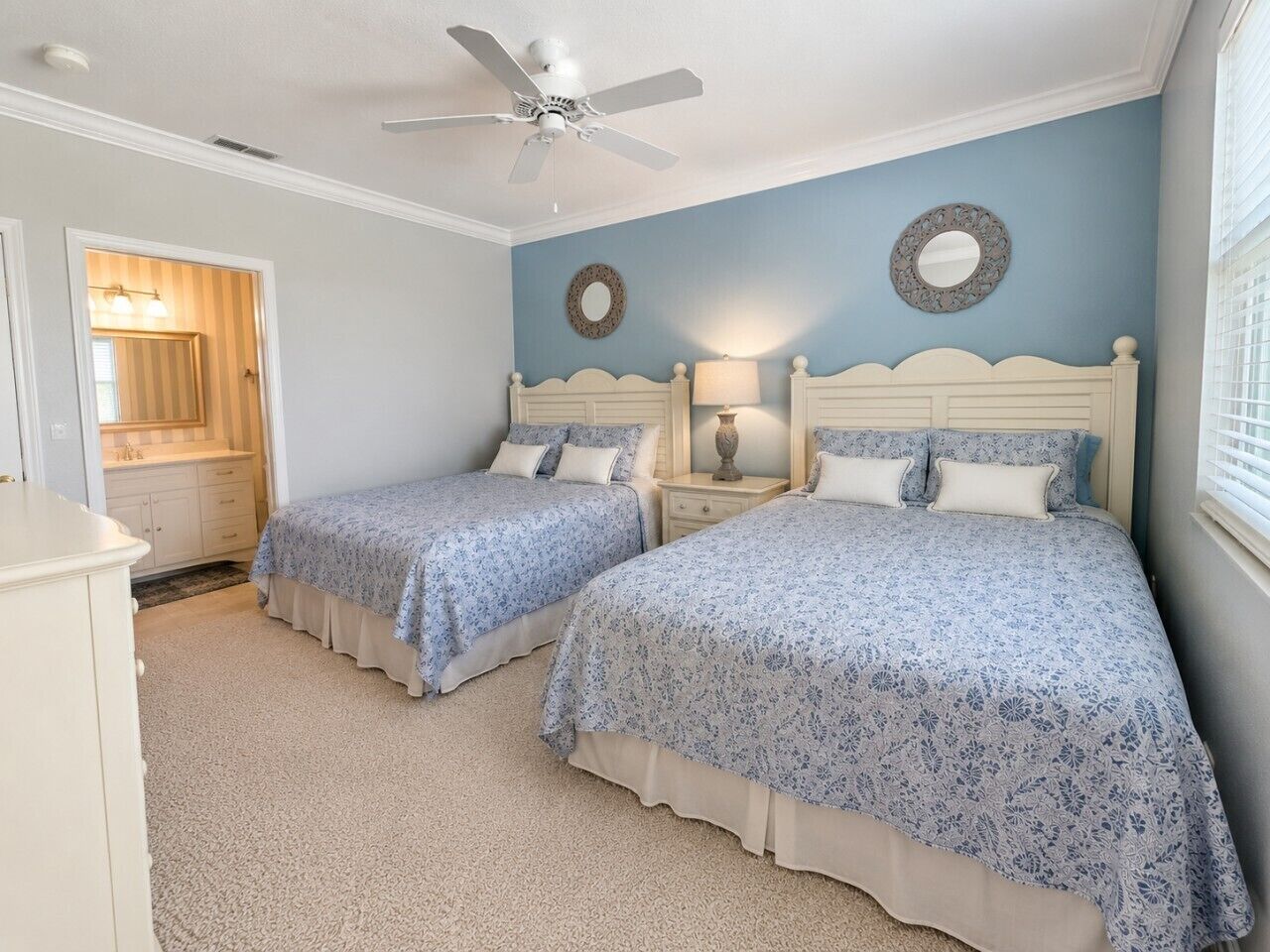 A bedroom with two beds, a ceiling fan, a nightstand with a lamp, and a mirror on the wall.