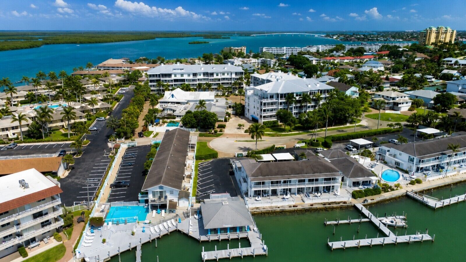 An aerial view of a coastal hotel area with multiple buildings, a marina, and a large swimming pool.