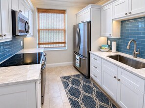 A kitchen with white cabinets, a stainless steel refrigerator, a black stove, a blue tiled backsplash, and a patterned rug. - Olde Marco Inn #403, Waterfront Island Escape (Marco Island)