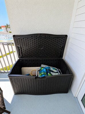 A black wicker storage box on a balcony with a clear view of a residential area and a building in the background. - Olde Marco Inn #403, Waterfront Island Escape (Marco Island)