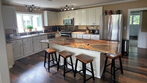 A modern kitchen with white cabinets, a large island with stools, stainless steel appliances, and a ceiling track lighting system. - Escape to Montana - Ranch-Style Home with Hot Tub & Mountain Views (Belgrade)