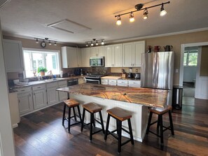 A modern kitchen with white cabinets, a large island with stools, stainless steel appliances, and a ceiling track lighting system.