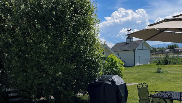 A hot tub with a clear view of the surrounding garden, a covered table, and a building in the background. - Escape to Montana - Ranch-Style Home with Hot Tub & Mountain Views (Belgrade)
