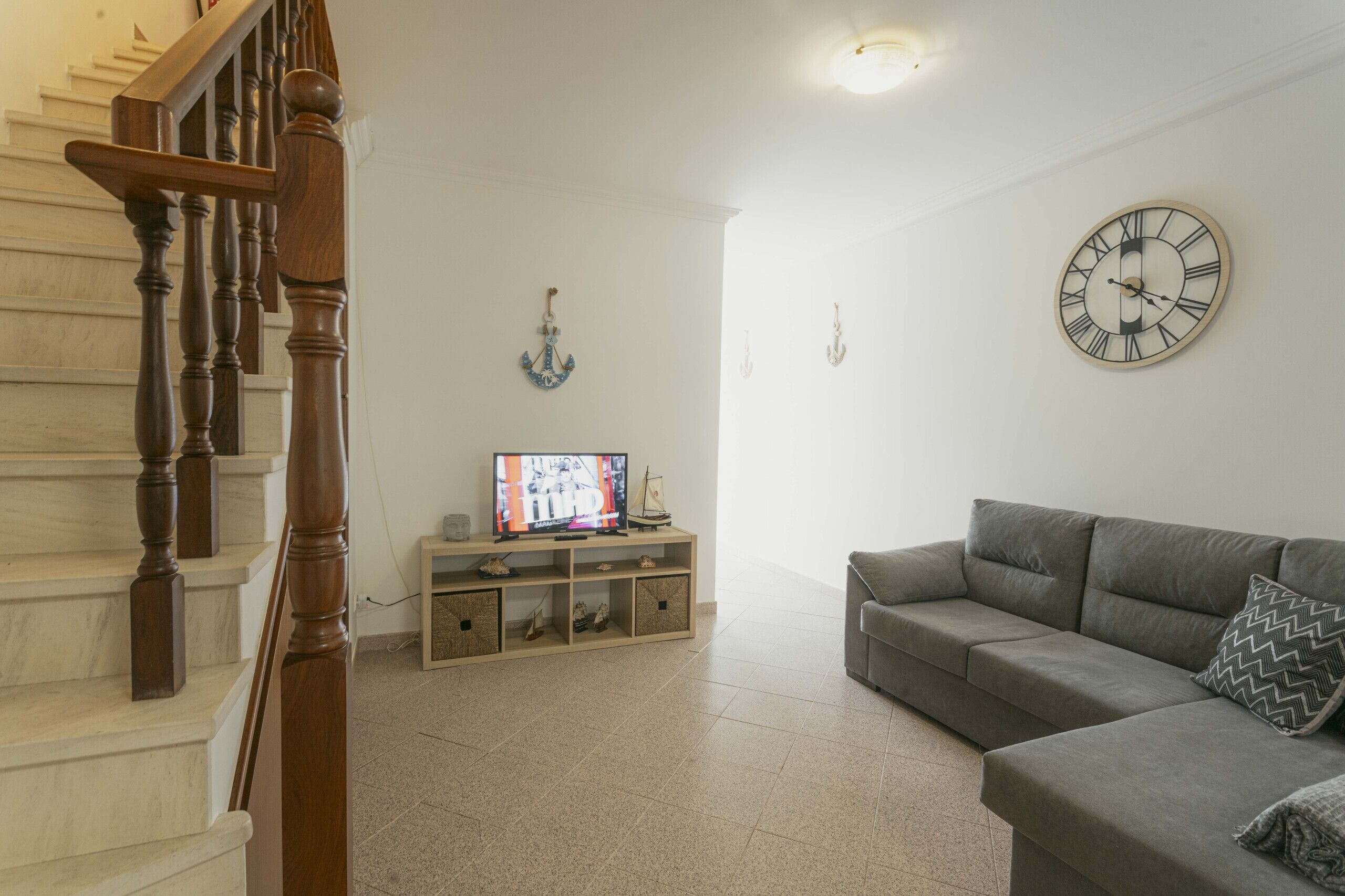 Een woonkamer met een trap, een televisie, een bank en een wandklok.