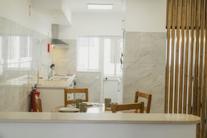 A modern kitchen with marble countertops, wooden chairs, and a dining table set for two. - Best Houses 15 - Vivenda Adelino Martins (Ferrel)