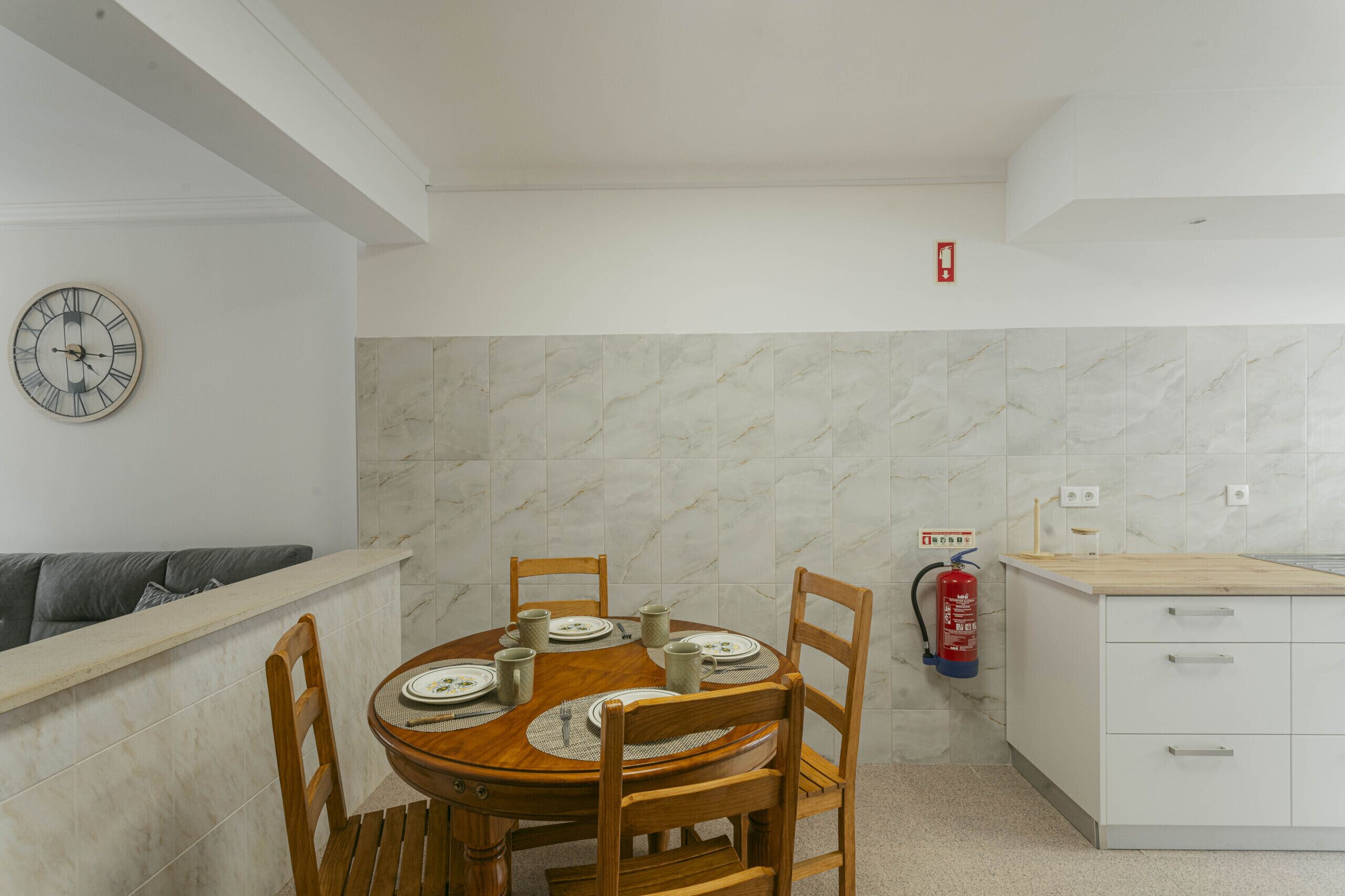 A dining area with a round table, chairs, plates, and a clock on the wall.