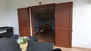 Eine offene Schiebetür führt in einen Essbereich mit Tisch und Stühlen, im Hintergrund ist eine Küche zu sehen, und auf dem Tisch steht ein Blumentopf.