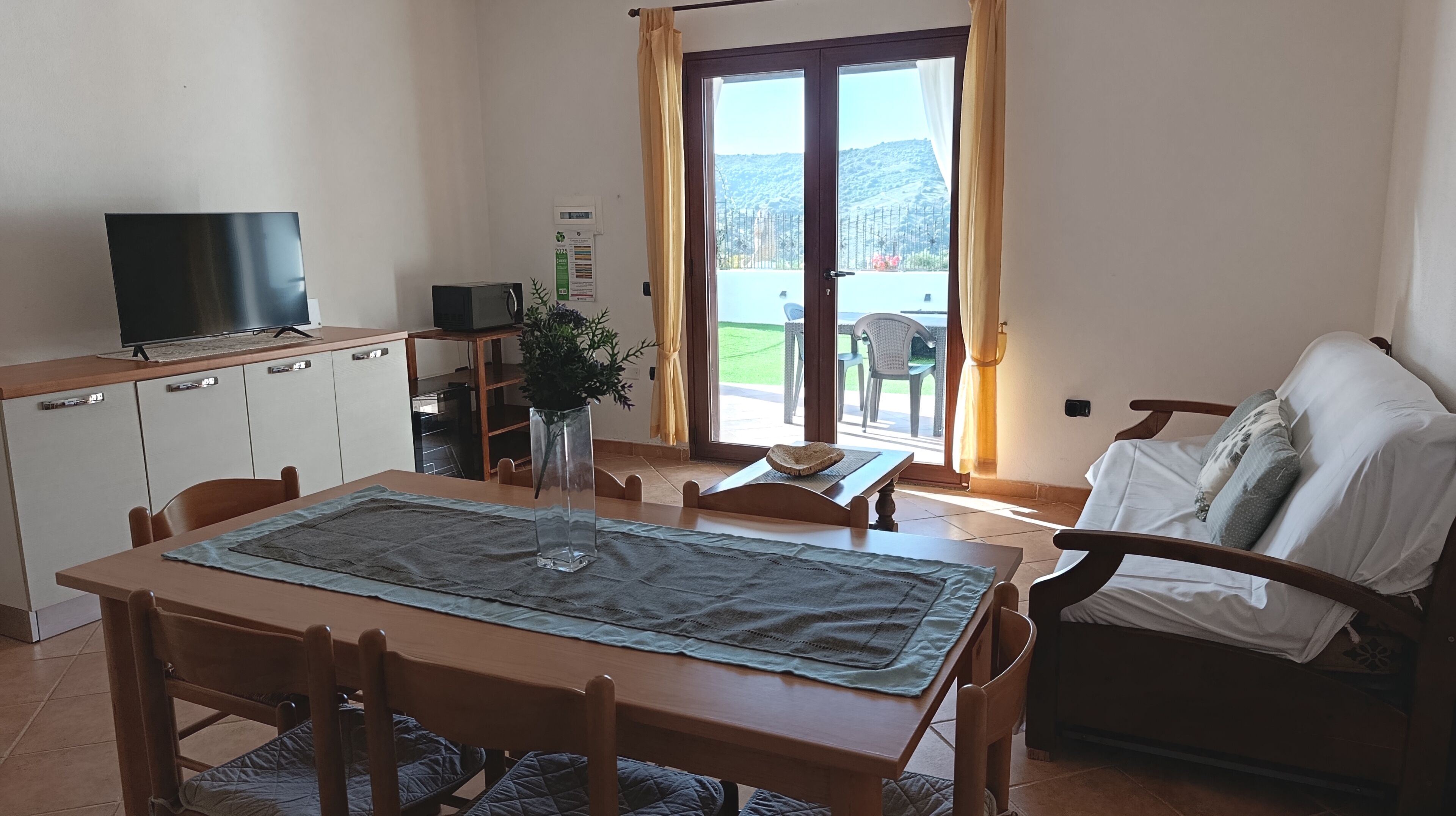 Ein Essbereich mit Tisch, Stühlen, einem Fernseher und Blick durch eine Glastür.