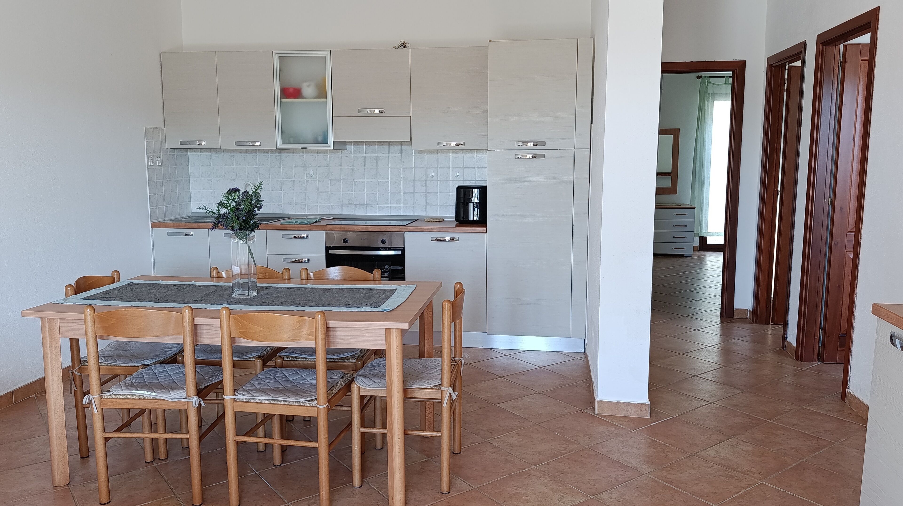 Een keuken met een eettafel en stoelen, een koffieapparaat en kastjes.