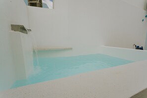 Ein Zimmer mit einer Badewanne voller Wasser, einem Fenster und einem am Wand montierten Wasserhahn.