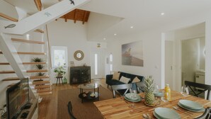 A spacious living area with a wooden staircase, a dining table set for two, and a cozy seating arrangement. - Best Houses 17 - Casa da Saudade (Geraldes)