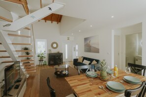 Ein geräumiger Wohnbereich mit einer Holztreppe, einem für zwei Personen gedeckten Esstisch und einer gemütlichen Sitzecke.
