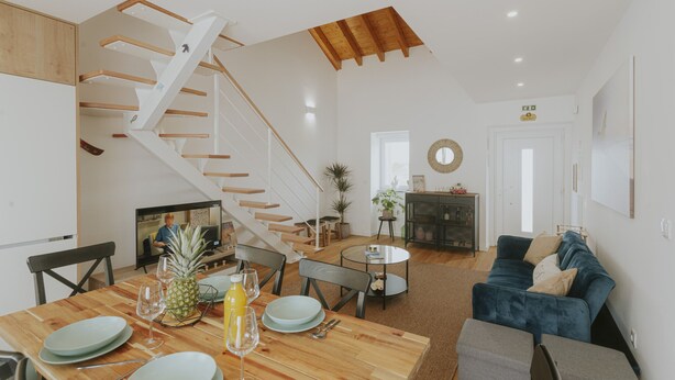 A spacious living area with a wooden dining table, a blue sofa, a staircase, and a round coffee table. - Best Houses 17 - Casa da Saudade (Geraldes)