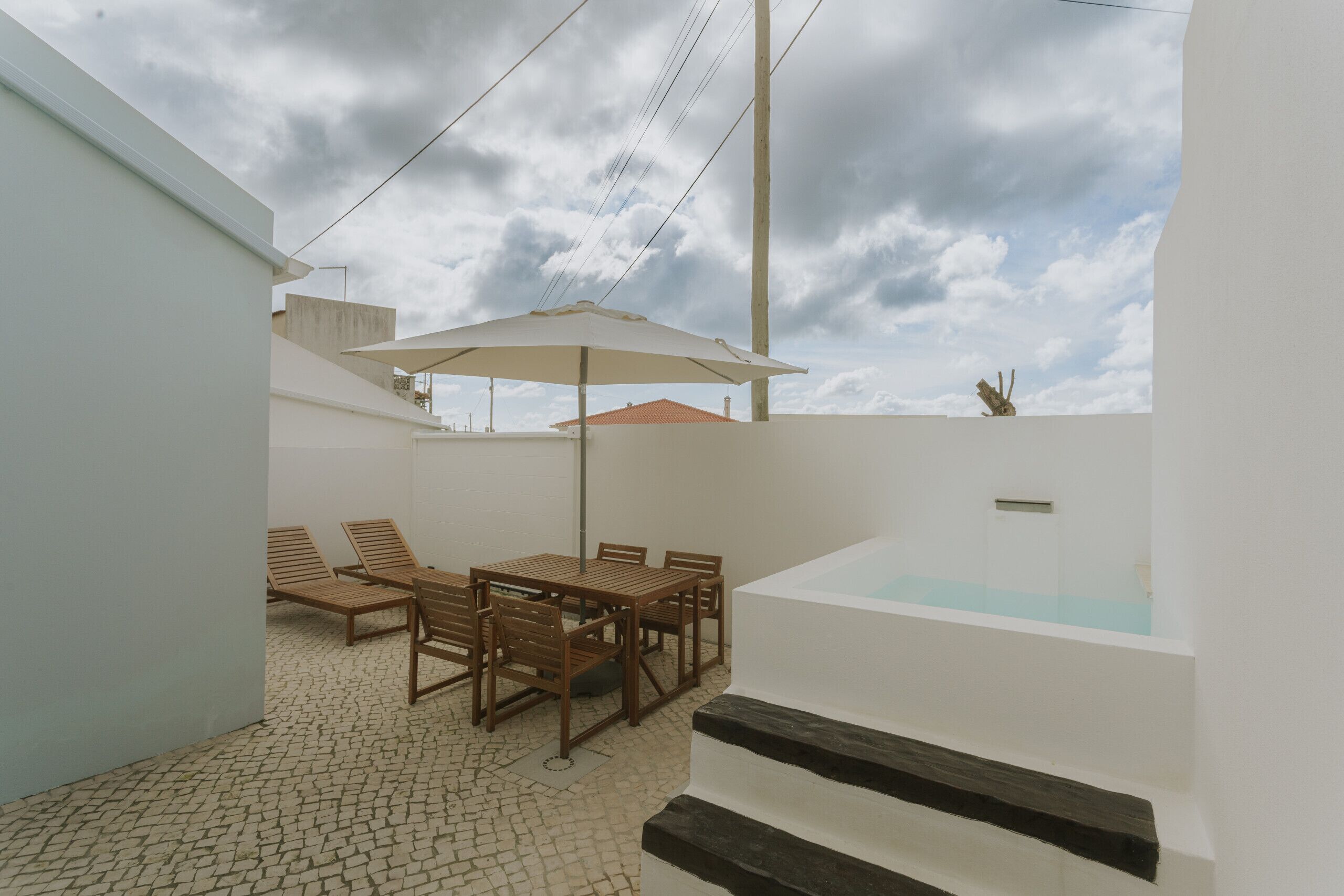 Une terrasse avec une table et des chaises, un parasol et un jacuzzi.
