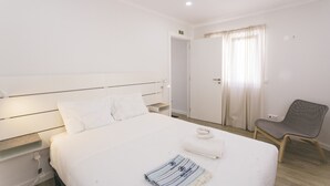 A hotel room with a bed, a chair, a door, and a wall-mounted light.