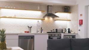 A modern kitchen with white cabinetry, stainless steel appliances, and a grey sofa in the foreground.