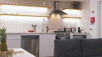 A modern kitchen with white cabinetry, stainless steel appliances, and a grey sofa in the foreground.