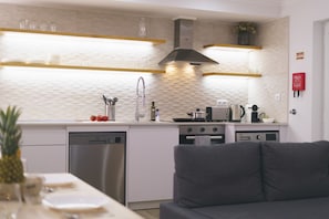 Una cocina moderna con armarios blancos, electrodomésticos de acero inoxidable y un sofá gris al frente.