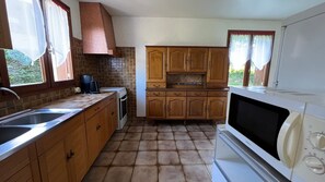Une cuisine avec des meubles de rangement en bois, une cuisinière, un four à micro-ondes, un évier et une fenêtre avec des rideaux.