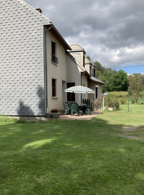 Une maison avec une façade en briques, un balcon et une terrasse équipée de chaises et d’un parasol.
