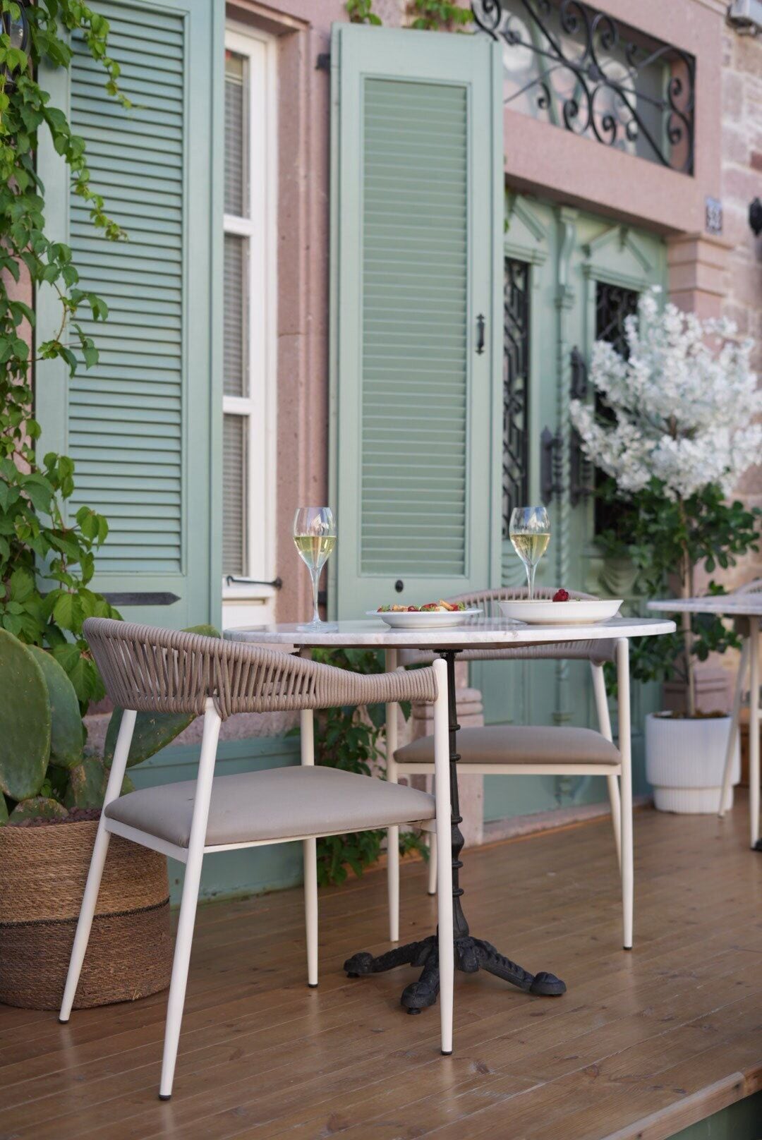 Una mesa con dos sillas, un plato de comida y dos copas de vino blanco en una terraza de madera.