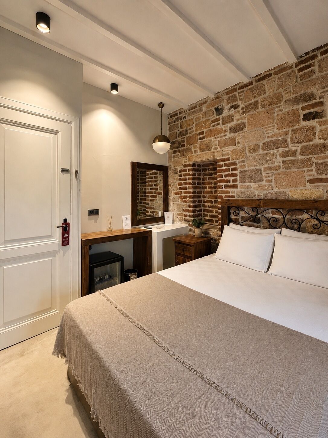 Un dormitorio con cama, cabecera de madera, pared de piedra, puerta blanca y un escritorio pequeño con espejo.