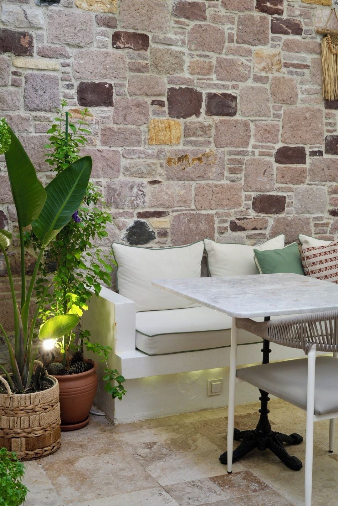 Ein gemütlicher Sitzbereich mit Steinwand, weißem Sofa, einem Tisch und Blumentöpfen.