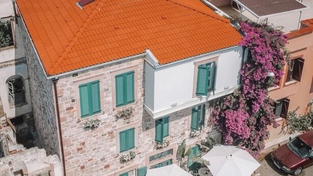 Un edificio de varios pisos con techo de tejas rojas, paredes de piedra y contraventanas verdes.