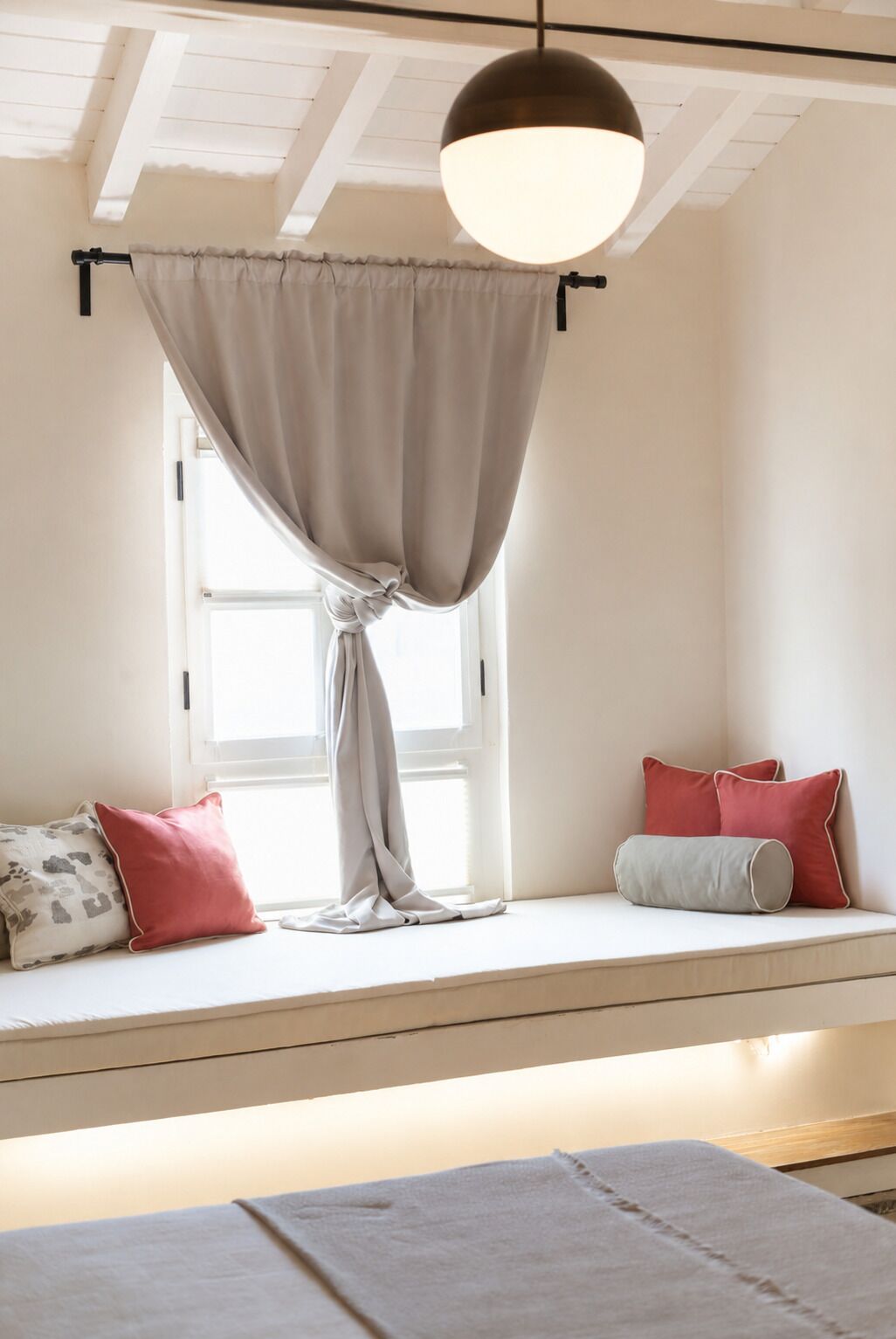 Een kamer met een raamzitje, een hanglamp en kussens.