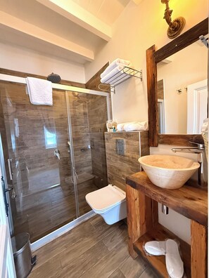 A modern bathroom with a glass-enclosed shower, a wooden vanity with a large basin, and a mirror with a decorative frame. - Galinis 1894 Cunda (Ayvalık)