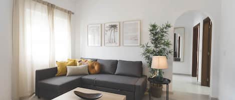Una sala de estar con un sofá, una mesita de centro, una lámpara y cuadros en la pared.