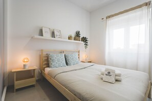 Ein Schlafzimmer mit einem hölzernen Bett, Nachttischlampen, einem Regal mit Dekoration und einem Fenster mit durchsichtigen Vorhängen.