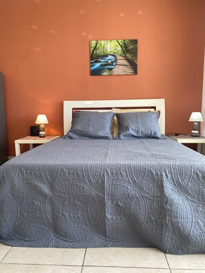 Ein Bett mit einem gemusterten Überwurf, zwei Kissen, einem Kopfteil und einem Wandbild einer Waldszene.