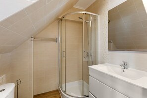 Un baño con cabina de ducha de vidrio, un lavabo blanco y un espejo.