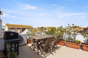 Terraza en la azotea con mesa y sillas, una parrilla y plantas en macetas.