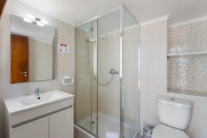 Un baño moderno con ducha envuelta en vidrio, lavamanos blanco y retrete.