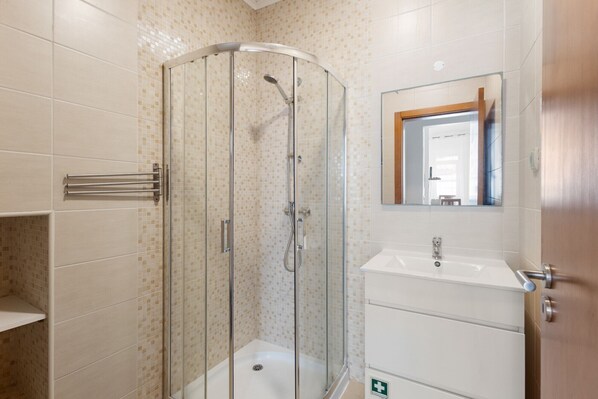 Un baño con ducha de vidrio, lavamanos y espejo.