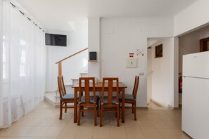 Ein Essbereich mit Tisch und Stühlen, einem Fernseher an der Wand, einem Rauchmelder und einem Kühlschrank.
