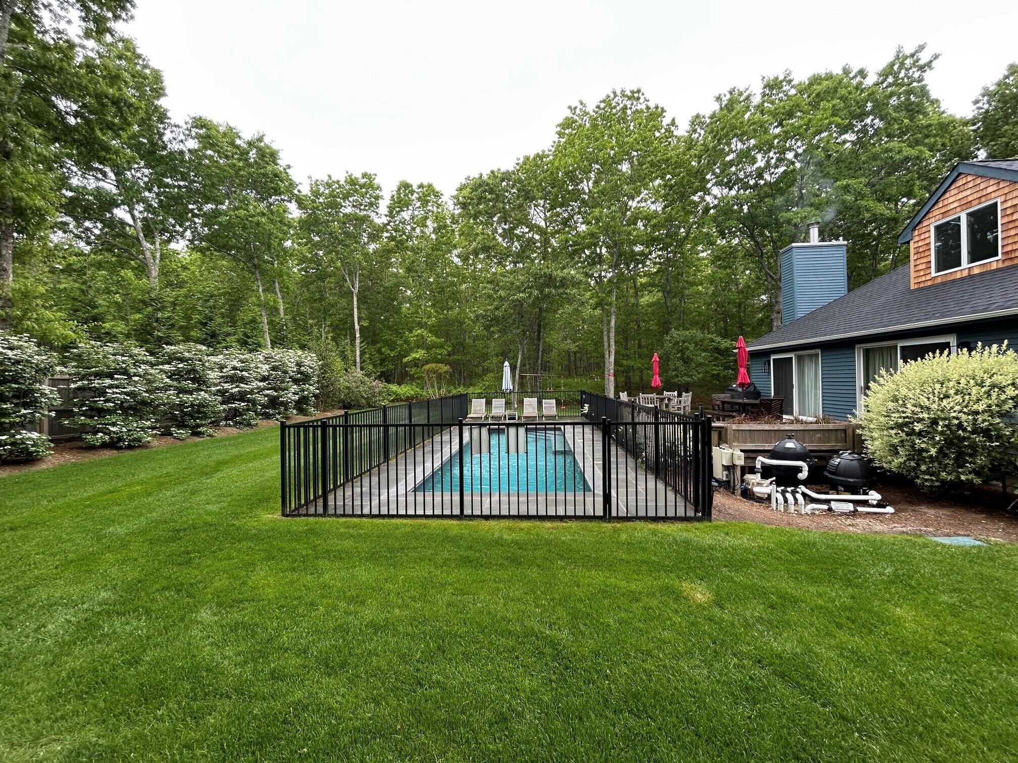 A backyard with a swimming pool, a wooden deck, and a house with a chimney.