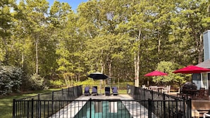 Ein Garten mit Swimmingpool, Liegestühlen und einer Grillgelegenheit.