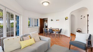 A living room with a sofa, chairs, a dining table, and a kitchen in the background. - Best Houses 91 - Casa D'el Rey (Amoreira)