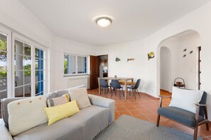 A living room with a sofa, chairs, a dining table, and a kitchen in the background. - Best Houses 91 - Casa D'el Rey (Amoreira)
